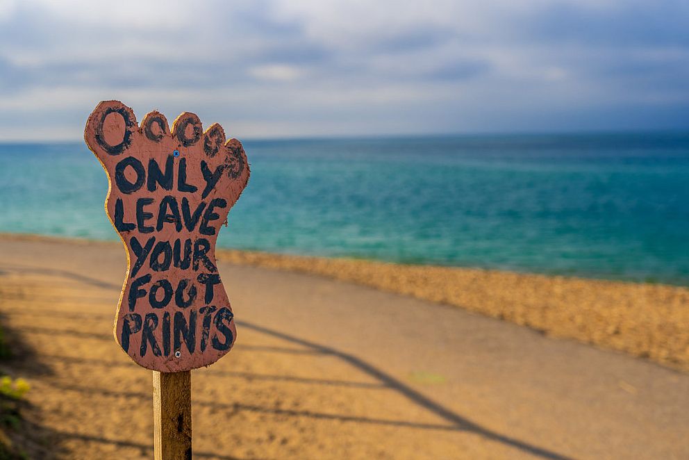 Schild in Fußform mit Aufschrift „Only leave your Footprint“ (Hinterlasse nur deine Fußabdrücke) am Strand.